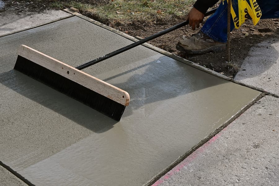 A concrete laborer uses a broom on wet "mud" concrete on a sidewalk repair project.