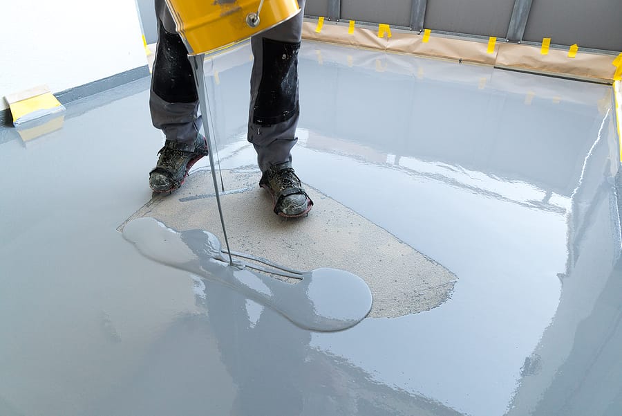 A construction worker renovates balcony floor and spreads watertight resin and glue before chipping and sealing